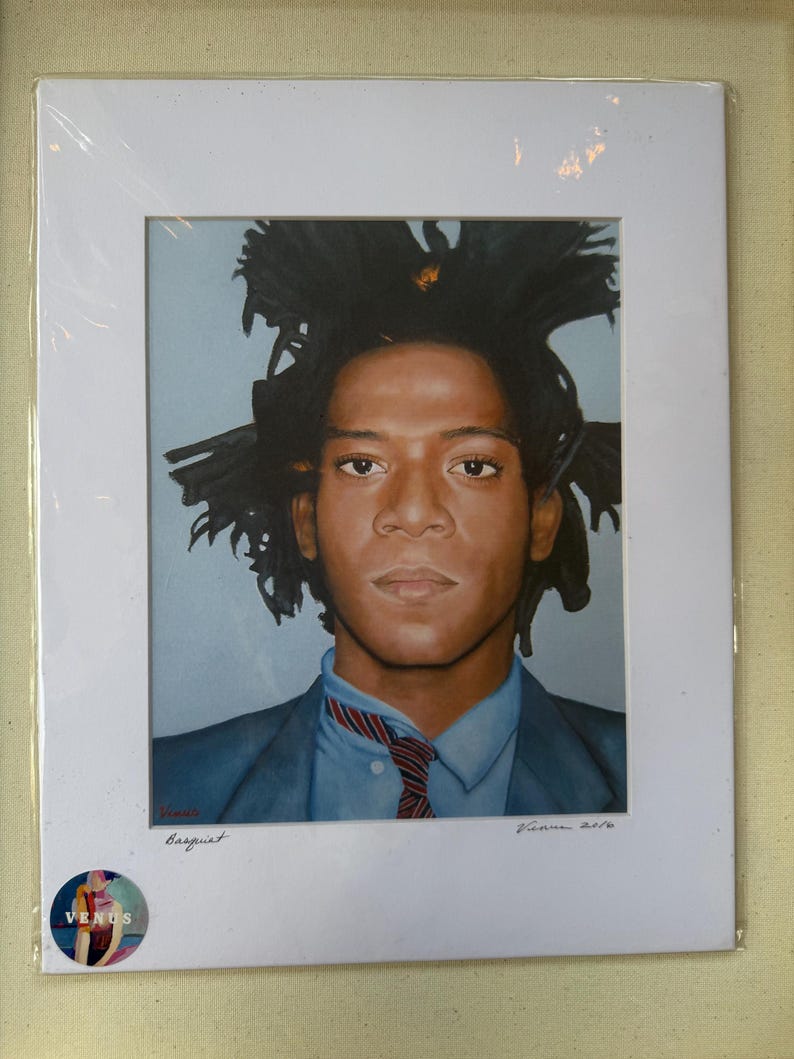 May include: A framed portrait of Jean-Michel Basquiat, depicting the artist in a blue suit and a red and blue striped tie. The artwork is signed and dated, with the word "Basquiat" written below the image. The frame is white.
