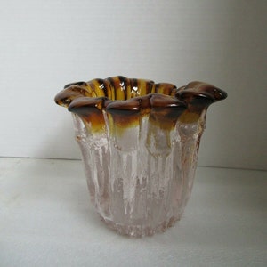 May include: A clear glass vase with a frosted, textured finish and a brown, amber-coloured rim. The vase has a unique, organic shape with a wide opening and a narrow base.