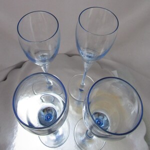 Puede incluir: Cuatro copas de vino transparentes con borde y base azules. Las copas est&aacute;n dispuestas en c&iacute;rculo, resaltando su elegante dise&ntilde;o. Los tallos son delgados y las copas ligeramente curvadas, perfectas para servir vino.