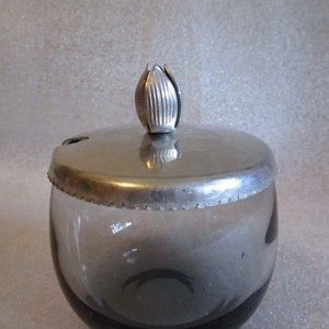 May include: A clear glass sugar bowl with a dark gray base and a silver lid with a decorative flower-shaped knob.