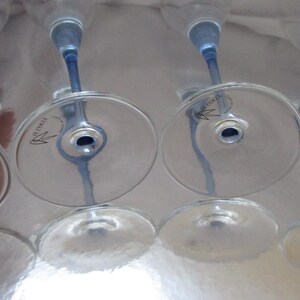 Puede incluir: Cuatro copas de vino transparentes con tallos y bases azules est&aacute;n dispuestas boca abajo. Las copas tienen un dise&ntilde;o delicado y est&aacute;n sobre una superficie reflectante. Los tallos son de color azul vibrante.