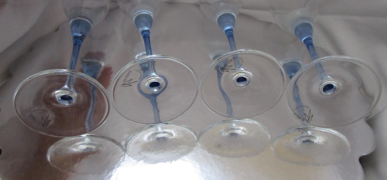 Puede incluir: Cuatro copas de vino transparentes con tallos y bases azules est&aacute;n dispuestas boca abajo. Las copas tienen un dise&ntilde;o delicado y est&aacute;n sobre una superficie reflectante. Los tallos son de color azul vibrante.
