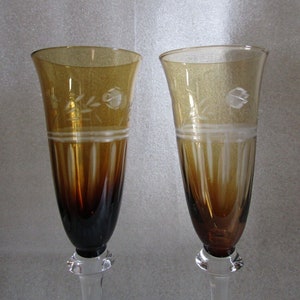 May include: Two amber-coloured champagne flutes with etched floral designs and clear stems.