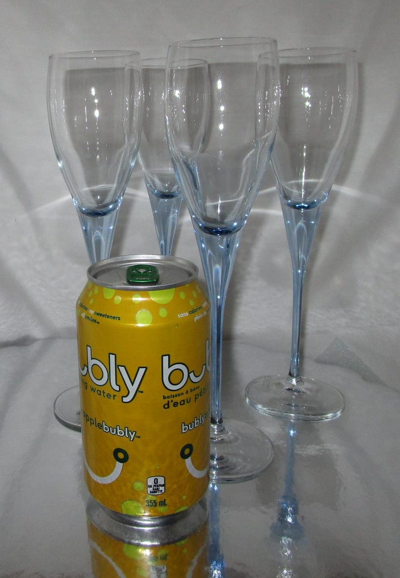 Puede incluir: Una lata amarilla de agua con gas Apple Bubly con cuatro copas de champ&aacute;n. Las copas tienen cuencos transparentes y tallos azul claro. La lata es de 355 ml.