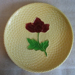 May include: A yellow ceramic plate with a raised design of a red flower with green leaves. The plate has a woven basket pattern.