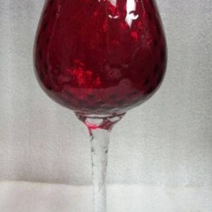 May include: A tall, clear glass vase with a red, textured, round bowl. The vase has a twisted stem and a clear base.