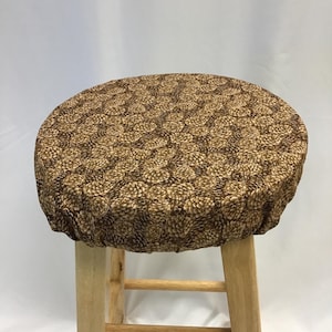 May include: A round wooden stool featuring a fabric cover with a repeating pattern of brown pinecones on a dark brown background. The stool has four light-coloured wooden legs connected by horizontal support bars near the base of the seat.