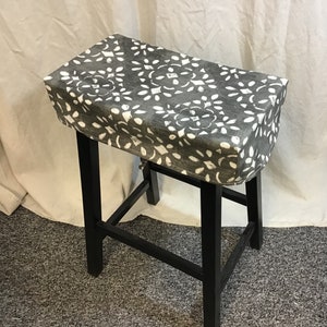 May include: A gray and white patterned fabric stool cover for a bar stool. The cover is made of a soft, durable fabric and has a simple, elegant design.