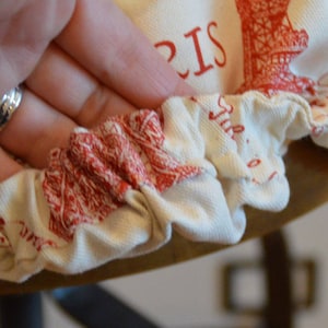 Pu&ograve; includere: Una fodera per sedia in tessuto bianco con un design della Torre Eiffel rossa e la parola "PARIGI" stampata su di essa. La fodera ha un bordo elastico arricciato.