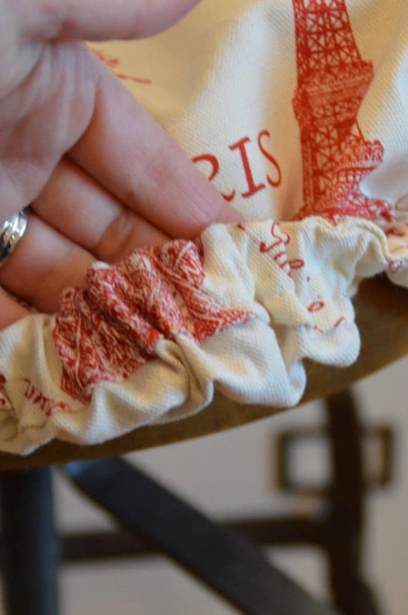 Pu&ograve; includere: Una fodera per sedia in tessuto bianco con un design della Torre Eiffel rossa e la parola "PARIGI" stampata su di essa. La fodera ha un bordo elastico arricciato.