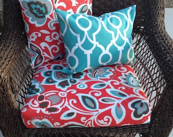 May include: A wicker swivel chair with a red, white, and turquoise floral patterned cushion and two throw pillows. One pillow has a turquoise and white geometric pattern, and the other has a red, white, and turquoise floral pattern.