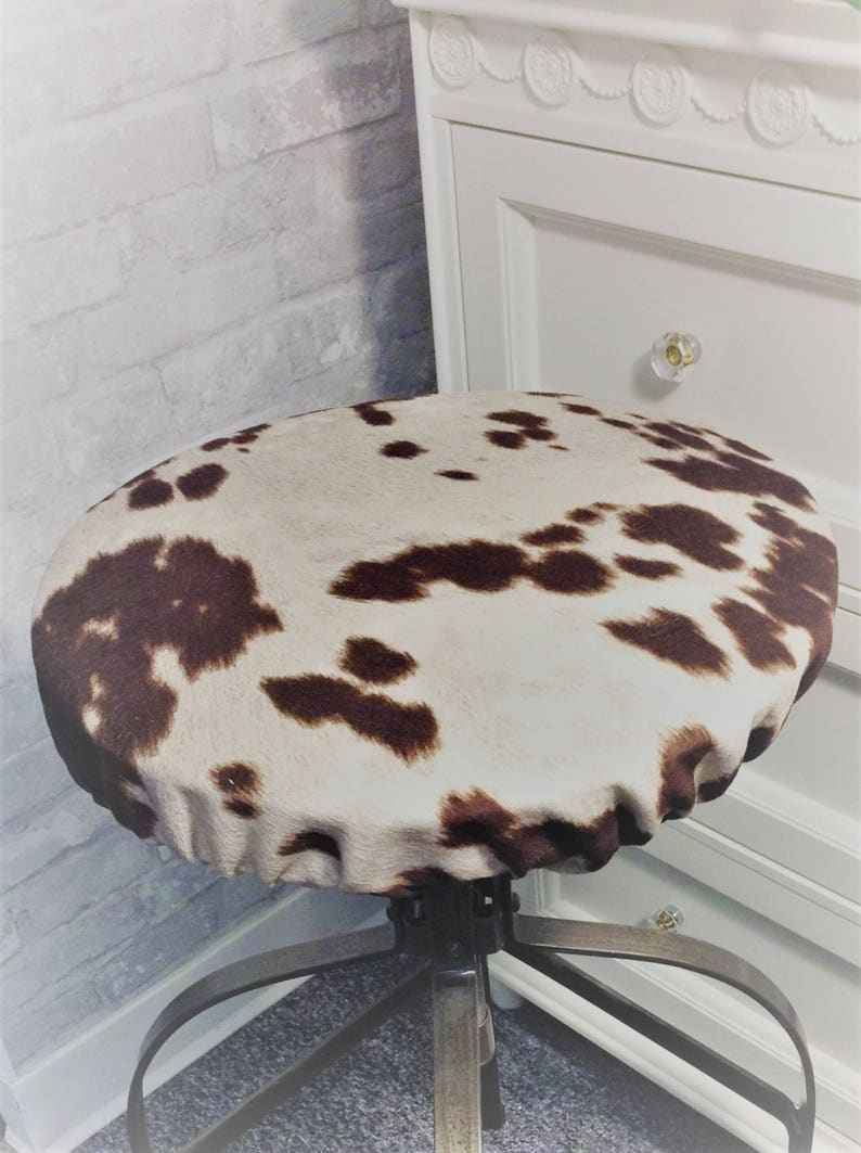 May include: A brown and white cowhide patterned chair seat cover. The cover is made of a soft, plush fabric and has a gathered edge.