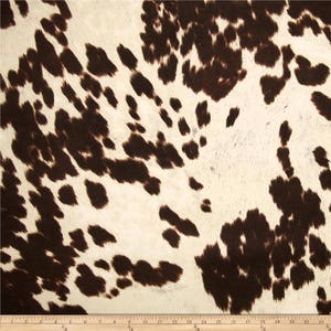 May include: Brown and white cowhide print fabric. The fabric has a soft, fuzzy texture.