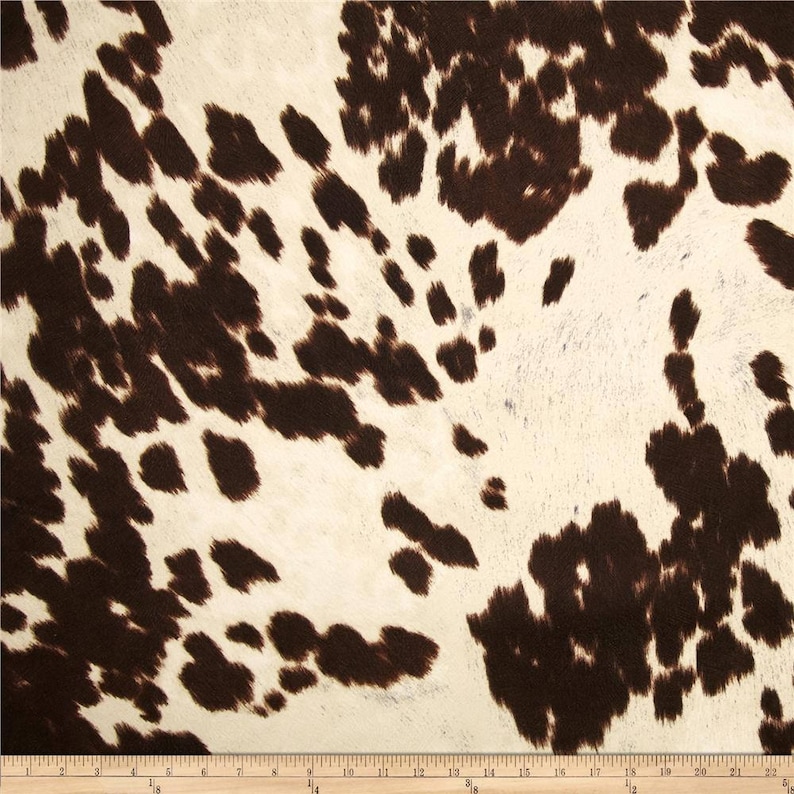 May include: Brown and white cowhide print fabric. The fabric has a soft, fuzzy texture.
