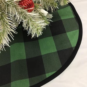 May include: A green and black buffalo plaid Christmas tree skirt with a black trim.