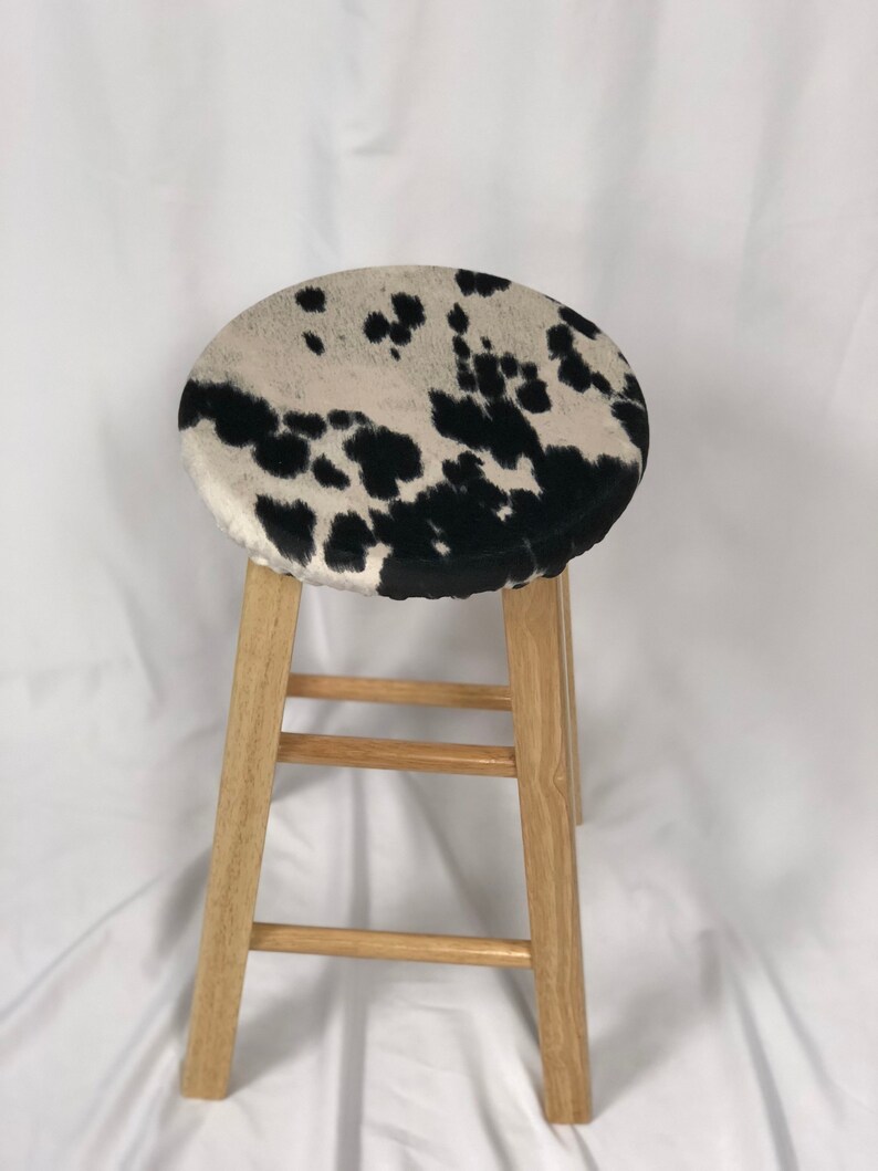 Pu&ograve; includere: Uno sgabello in legno con un cuscino per la seduta in pelle di mucca bianco e nero.
