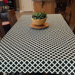 May include: Black and white checkered tablecloth with a woven pattern. The tablecloth is laid out on a wooden table with a potted plant in the center.