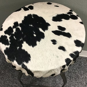 May include: A round, black and white cowhide table top with a black metal base.
