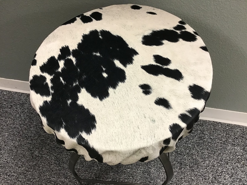 Pu&ograve; includere: Un piano da tavolo rotondo in pelle di mucca bianca e nera con una base in metallo nero.