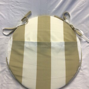 May include: Round chair cushion with a beige and white striped pattern. The cushion has ties on each side to secure it to a chair.