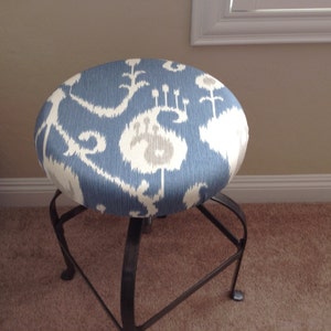 Könnte beinhalten: Ein blauer und weißer Stoffhocker mit einem schwarzen Metallgestell. Der Hocker hat eine runde Sitzfläche und ein schlichtes Design.