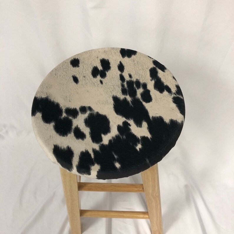 Pu&ograve; includere: Uno sgabello da bar in legno con un cuscino per la seduta in pelle di mucca bianco e nero.
