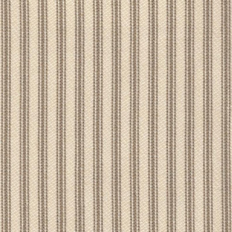 May include: A woven fabric featuring a repeating pattern of vertical stripes in a neutral taupe color against a light cream background. The texture of the material is visible, showing a consistent weave throughout the entire surface of the textile.