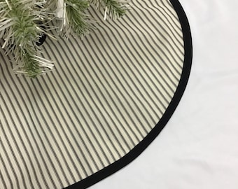 May include: A black and white striped Christmas tree skirt with a black trim. The skirt is made of fabric and has a round shape.