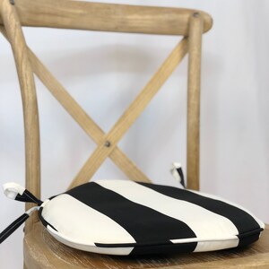 May include: A black and white striped round chair cushion with a tie closure. The cushion is sitting on a wooden chair.