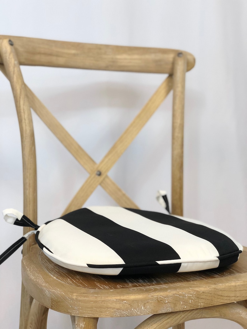 May include: A black and white striped round chair cushion with a tie closure. The cushion is sitting on a wooden chair.