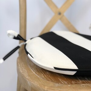 May include: A black and white striped round chair cushion with a tie closure. The cushion is sitting on a wooden chair.