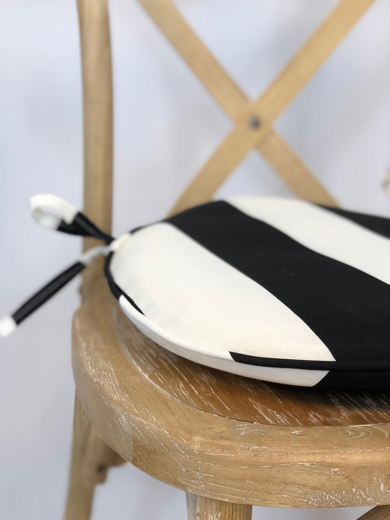 May include: A black and white striped round chair cushion with a tie closure. The cushion is sitting on a wooden chair.