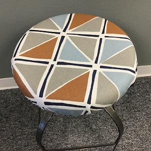 May include: A round stool with a grey, blue and orange geometric pattern fabric seat cover. The stool has a metal frame.