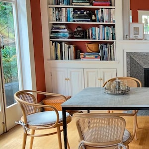 May include: A dining area featuring a square marble-topped table with a black metal frame and two light-colored wooden chairs with woven cane backs and light gray tie-on seat cushions. A silver tray with glassware sits on the table surface.