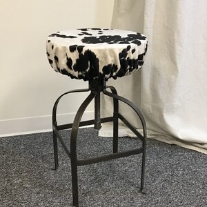 Pu&ograve; includere: Uno sgabello con un motivo a pelle di mucca bianco e nero e una base in metallo. Lo sgabello &egrave; regolabile in altezza.
