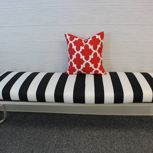 May include: A white bench with black stripes on the seat and scrolled metal legs. A red cushion with a white geometric pattern is on the seat.