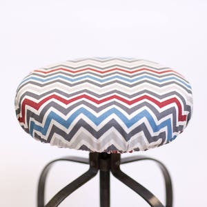 May include: A gray, blue, and red chevron patterned chair seat cover. The cover is made of fabric and has a gathered edge.