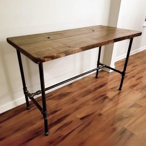 May include: A rustic wooden table with a black metal pipe frame. The table has a natural wood finish and is supported by four black metal pipes.