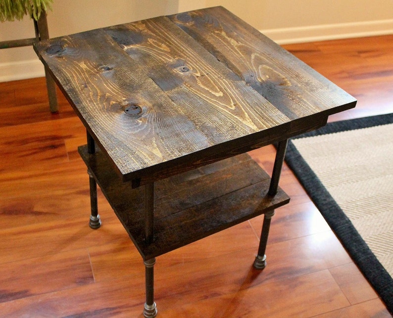 May include: A dark brown wooden end table with a lower shelf and black metal pipe legs. The table is sitting on a hardwood floor.