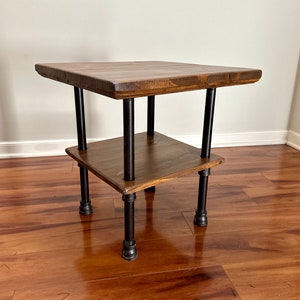 May include: A small wooden end table with a black metal frame. The table has two shelves and a square top.