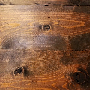 May include: Close-up of a dark brown wood surface with a natural wood grain pattern. The surface has a few knots and is slightly uneven.