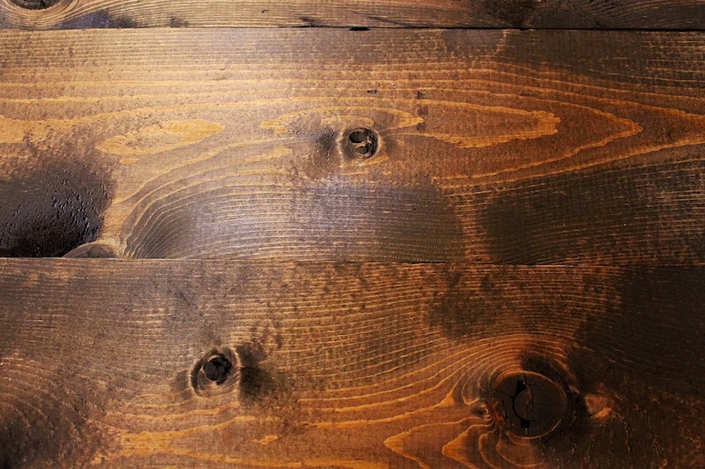 May include: Close-up of a dark brown wood surface with a natural wood grain pattern. The surface has a few knots and is slightly uneven.