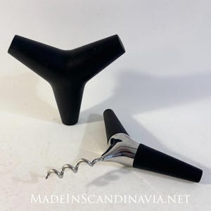 以下が含まれることがあります： 白い背景に、黒いY字型のボトルストッパーと、黒とシルバーのコルクスクリューの2つのワインアクセサリーが表示されています。コルクスクリューは銀色の螺旋と黒いハンドルを備えています。