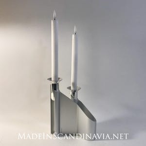 May include: A silver candle holder with two white candles. The holder has a modern design with a rectangular base and two vertical arms.