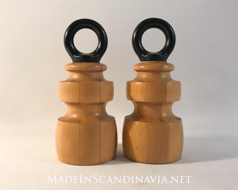 May include: Two wooden door stops with a natural wood finish and black ring handles. The door stops have a turned design and are displayed against a white background. The text "MADEINSCANDINAVIA.NET" is visible at the bottom.