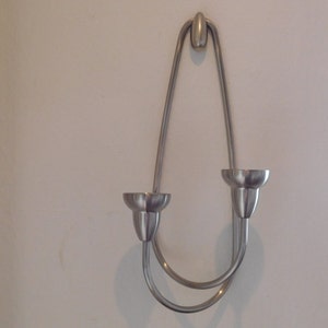 Può includere: Portacandele da parete in argento con due portacandele. Il portacandele è realizzato in un unico pezzo di metallo piegato a forma di U.