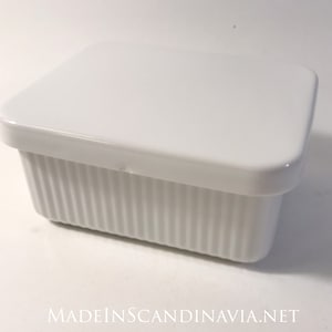 Può includere: Un porta burro in ceramica bianca con coperchio. Il porta burro ha un design a coste e il coperchio è liscio.
