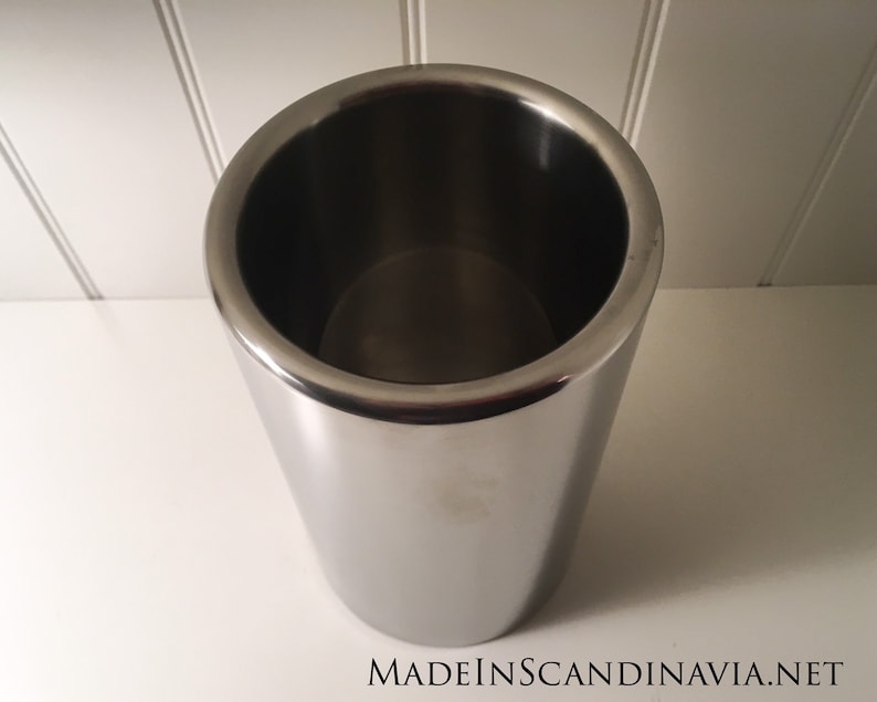 May include: A stainless steel wine chiller with a polished finish. The cylindrical container has a wide opening and a slightly tapered body. The text "MADEINSCANDINAVIA.NET" is visible at the bottom.