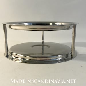 Puede incluir: Un soporte de metal plateado con dos niveles circulares. El soporte está hecho de metal pulido y tiene un diseño simple y moderno.