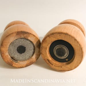 May include: Two wooden salt and pepper grinders with a light wood finish. The grinders have a rounded shape with a small knob on top and a metal mesh or grinding mechanism on the bottom. The text "MADEINSCANDINAVIA.NET" is at the bottom.